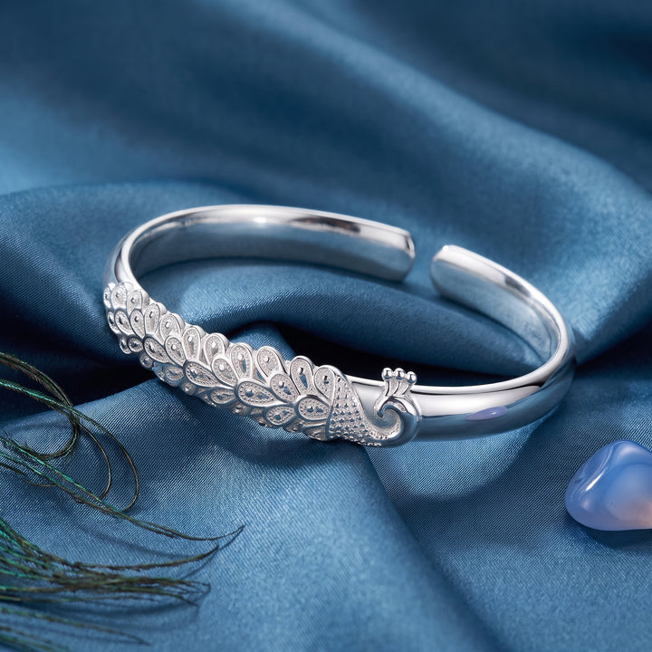 Open silver peacock plume cuff bracelet on blue satin